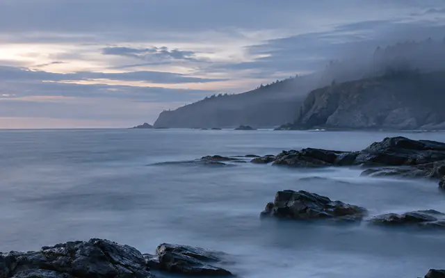 A misty headland above a calm sea at blue hour